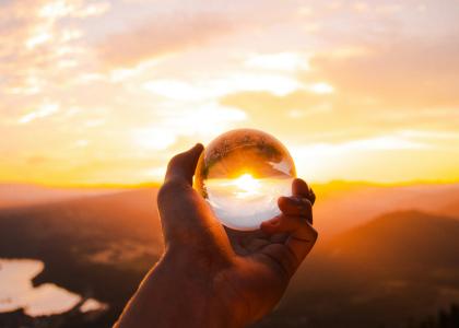Hand holding crystal ball reflecting the sunset