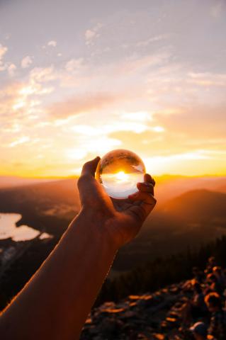 Hand holding crystal ball reflecting the sunset